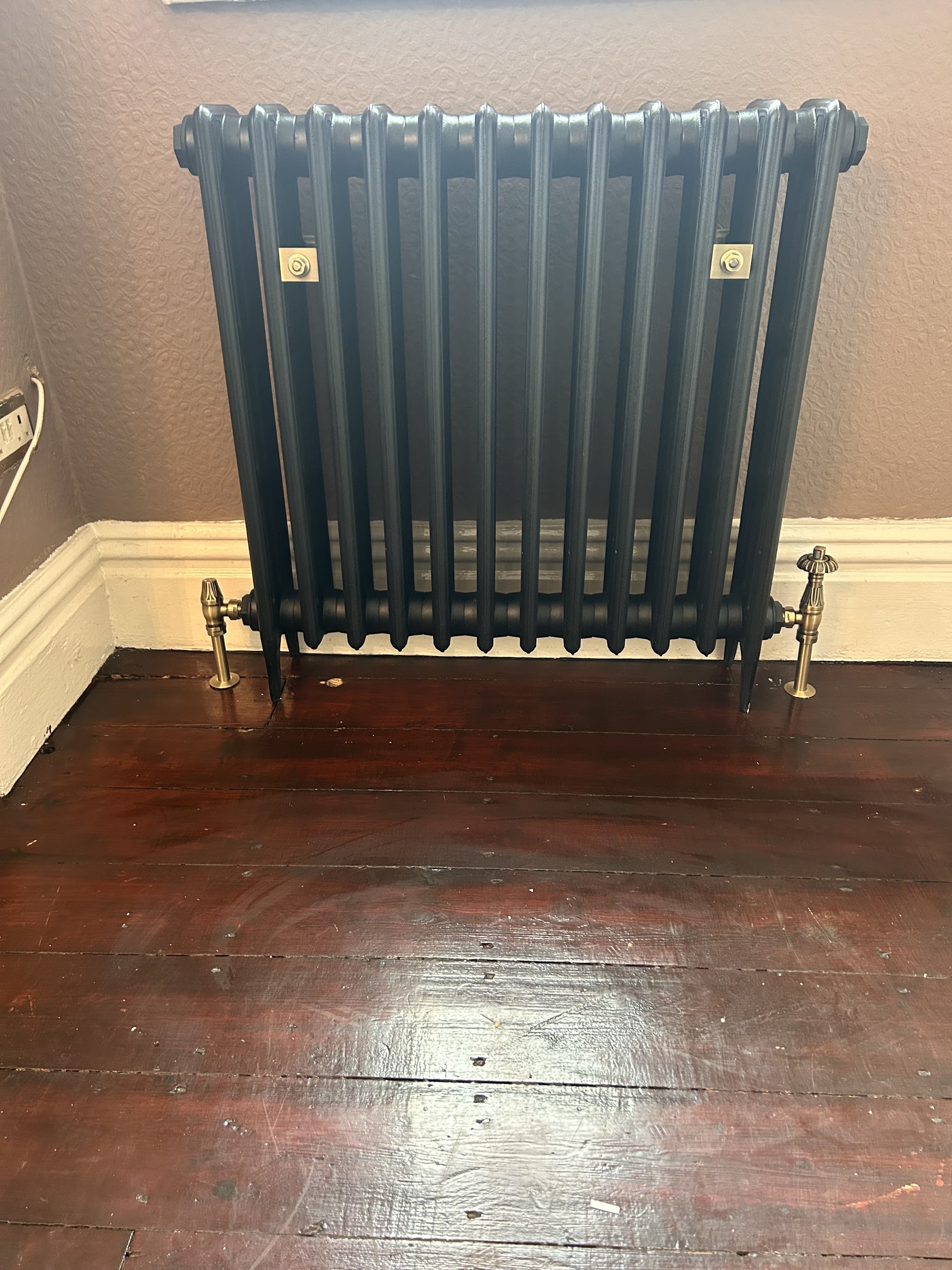 A cast-iron column radiator fitted on stripped floorboards
